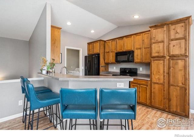 kitchen featuring a breakfast bar area, kitchen peninsula, independent washer and dryer, and black appliances