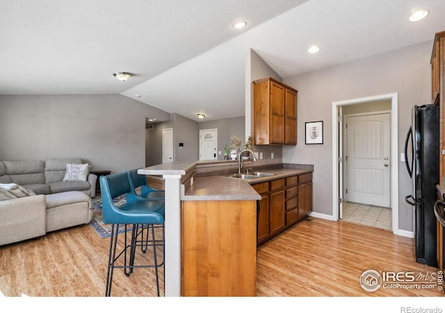 kitchen with vaulted ceiling, black refrigerator, sink, a kitchen breakfast bar, and kitchen peninsula