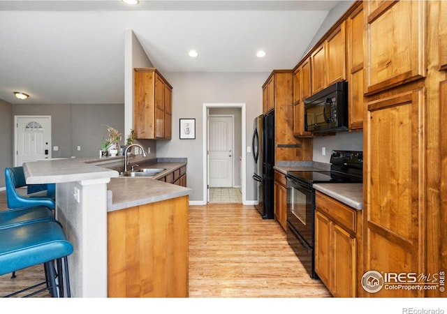 kitchen with sink, black appliances, a kitchen bar, kitchen peninsula, and light wood-type flooring