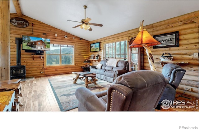 living room with rustic walls, high vaulted ceiling, a wood stove, hardwood / wood-style flooring, and ceiling fan