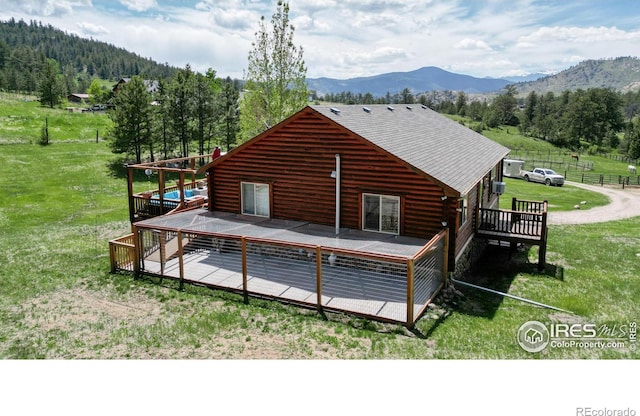 back of property with a deck with mountain view and a lawn