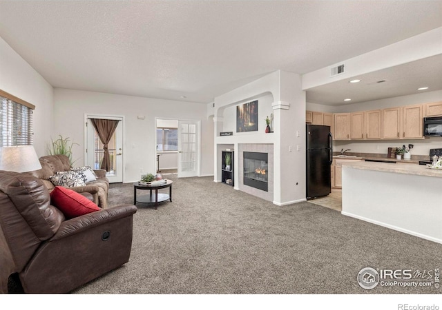 living room with a tiled fireplace, sink, light carpet, and a textured ceiling