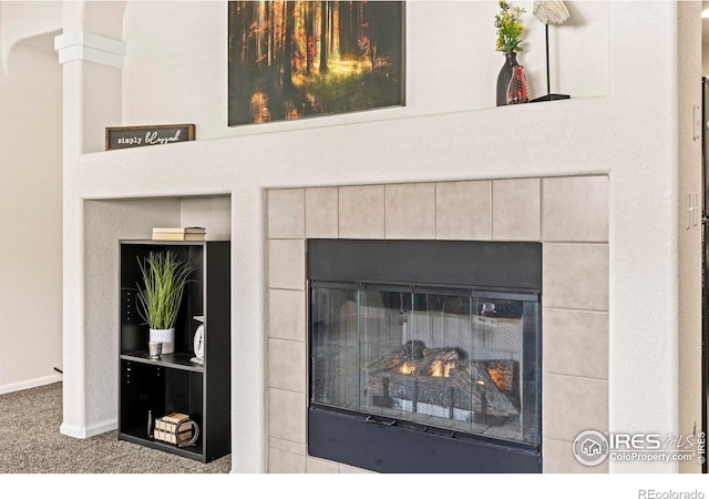 interior details featuring a tiled fireplace and carpet