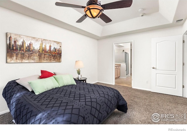 carpeted bedroom with ceiling fan, ensuite bathroom, and a raised ceiling