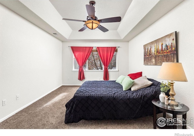 bedroom with a raised ceiling, ceiling fan, and carpet flooring