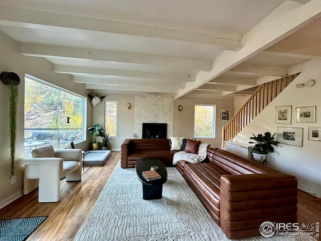 living room featuring beam ceiling, wood-type flooring, and a large fireplace