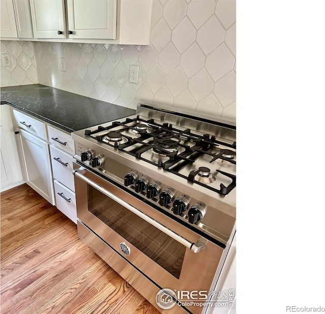 kitchen featuring white cabinetry, light hardwood / wood-style flooring, stainless steel stove, dark stone counters, and decorative backsplash