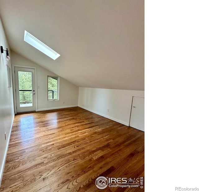 additional living space featuring wood-type flooring and lofted ceiling with skylight