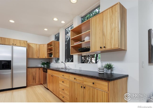 kitchen with appliances with stainless steel finishes, light hardwood / wood-style floors, sink, and dark stone countertops