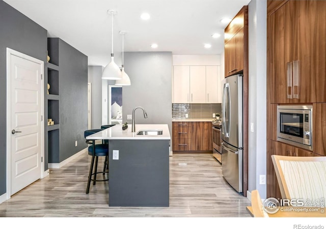 kitchen with sink, white cabinetry, hanging light fixtures, stainless steel appliances, and a kitchen island with sink