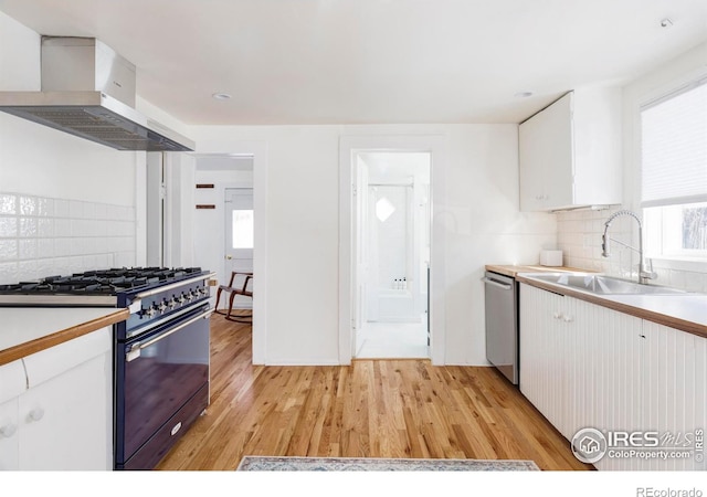 kitchen with white cabinetry, gas stove, sink, and wall chimney exhaust hood