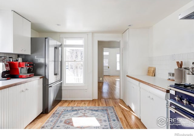 kitchen with range, stainless steel fridge, light hardwood / wood-style floors, decorative backsplash, and white cabinets