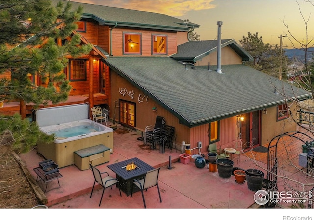 back house at dusk featuring a hot tub and a fire pit