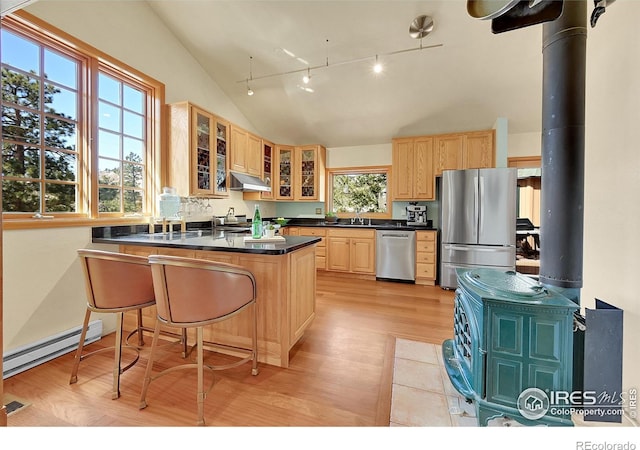 kitchen featuring lofted ceiling, a baseboard heating unit, stainless steel appliances, kitchen peninsula, and a wood stove