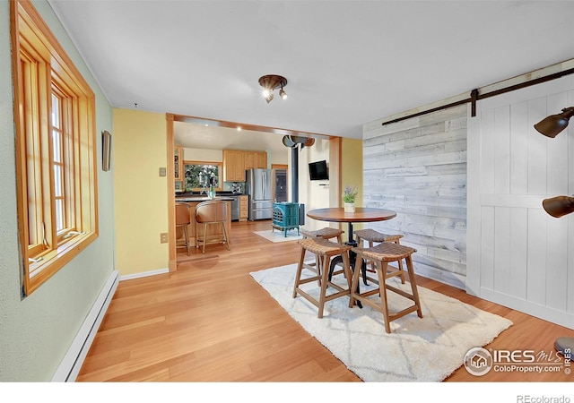 dining area featuring a baseboard radiator, a healthy amount of sunlight, light wood-type flooring, and a wood stove