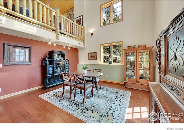 dining area with wood-type flooring, rail lighting, and a high ceiling