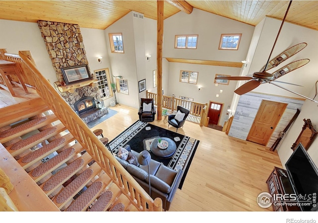 living room featuring high vaulted ceiling, a stone fireplace, wood ceiling, and light hardwood / wood-style floors