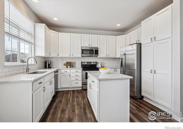 kitchen with a kitchen island, appliances with stainless steel finishes, sink, white cabinets, and backsplash