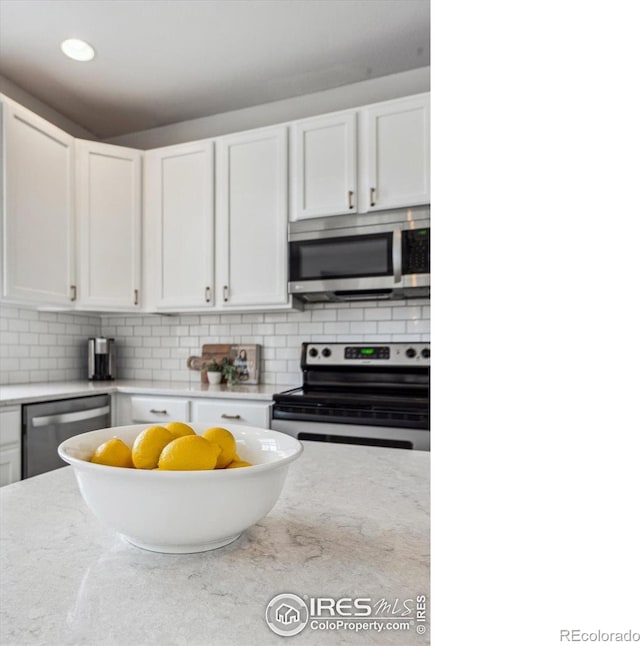 kitchen featuring white cabinetry, appliances with stainless steel finishes, light stone counters, and backsplash