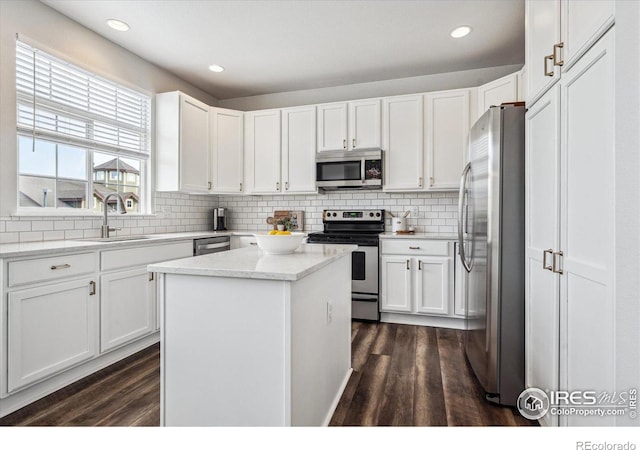 kitchen with sink, appliances with stainless steel finishes, backsplash, white cabinets, and a kitchen island