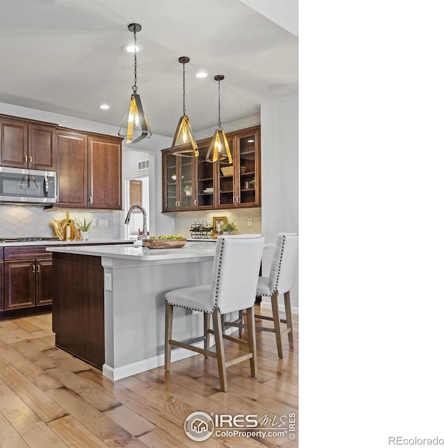 kitchen featuring decorative light fixtures, backsplash, a kitchen breakfast bar, dark brown cabinets, and light hardwood / wood-style flooring