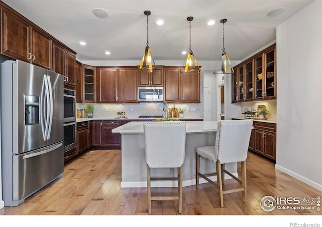 kitchen with hanging light fixtures, stainless steel appliances, light hardwood / wood-style floors, and a kitchen island