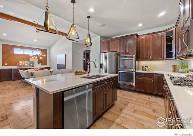 kitchen featuring appliances with stainless steel finishes, decorative light fixtures, sink, a kitchen island with sink, and dark brown cabinetry