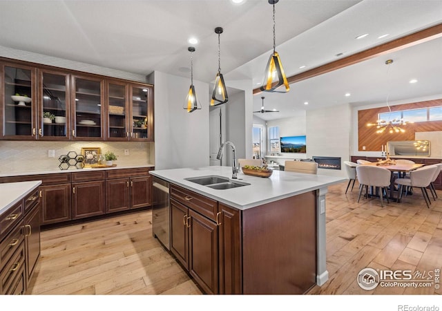 kitchen with an island with sink, sink, light wood-type flooring, and decorative light fixtures