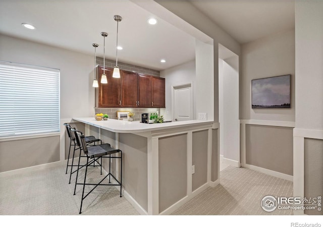 kitchen featuring a kitchen bar, decorative light fixtures, light carpet, kitchen peninsula, and decorative backsplash