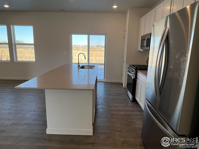 kitchen with appliances with stainless steel finishes, white cabinetry, an island with sink, sink, and dark wood-type flooring