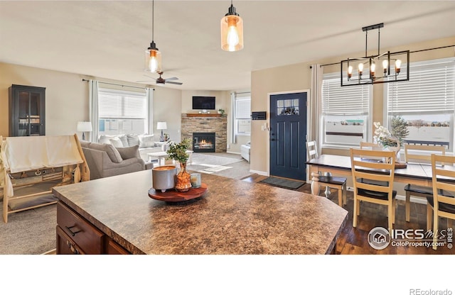 kitchen featuring ceiling fan with notable chandelier, a fireplace, decorative light fixtures, and dark wood-type flooring