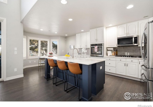 kitchen featuring stainless steel appliances, a breakfast bar, a center island with sink, and white cabinets