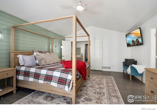 bedroom featuring dark hardwood / wood-style flooring, vaulted ceiling, wooden walls, and ceiling fan