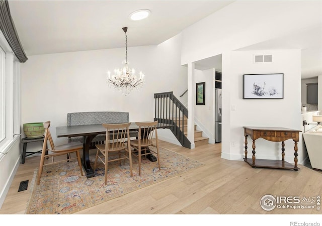 dining space featuring vaulted ceiling, a notable chandelier, and light hardwood / wood-style flooring