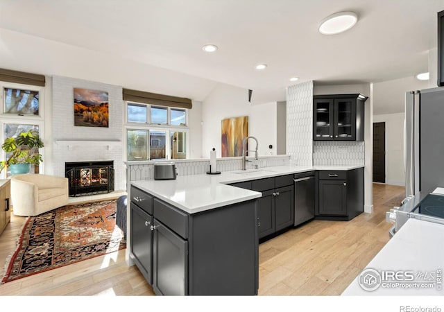 kitchen with sink, light hardwood / wood-style flooring, appliances with stainless steel finishes, a fireplace, and kitchen peninsula