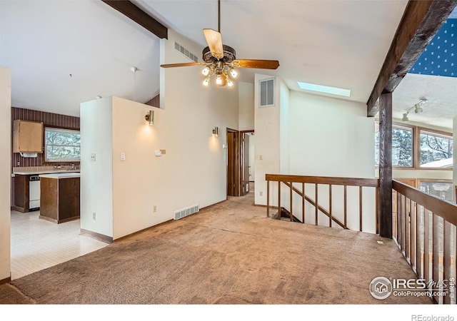 empty room featuring light colored carpet, beam ceiling, a skylight, and high vaulted ceiling