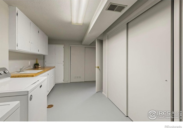 washroom with cabinets, sink, washing machine and dryer, and a textured ceiling