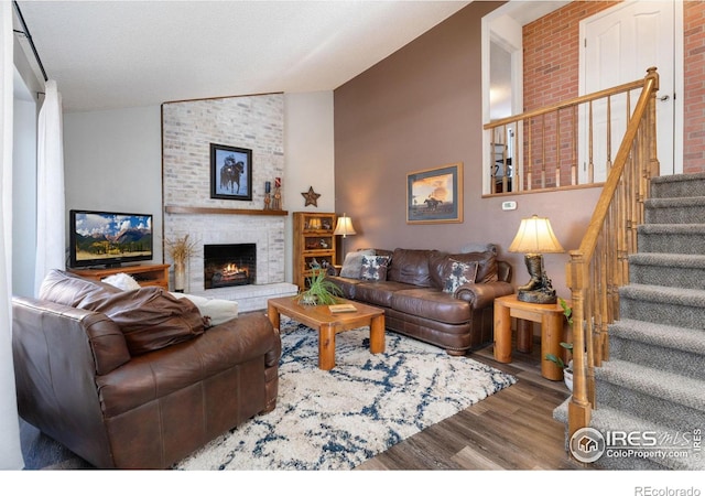 living room featuring vaulted ceiling, a brick fireplace, and wood-type flooring