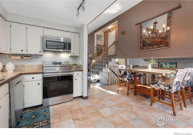 kitchen featuring pendant lighting, an inviting chandelier, stainless steel appliances, track lighting, and white cabinets