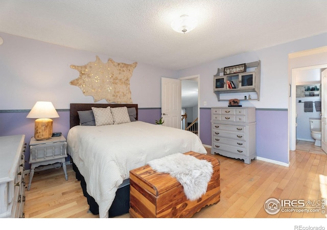 bedroom featuring ensuite bathroom, a textured ceiling, and light hardwood / wood-style flooring