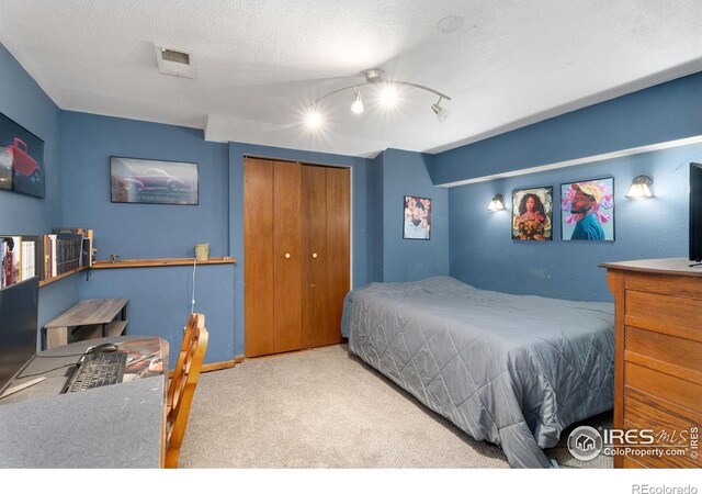 bedroom featuring track lighting, ceiling fan, light carpet, a textured ceiling, and a closet