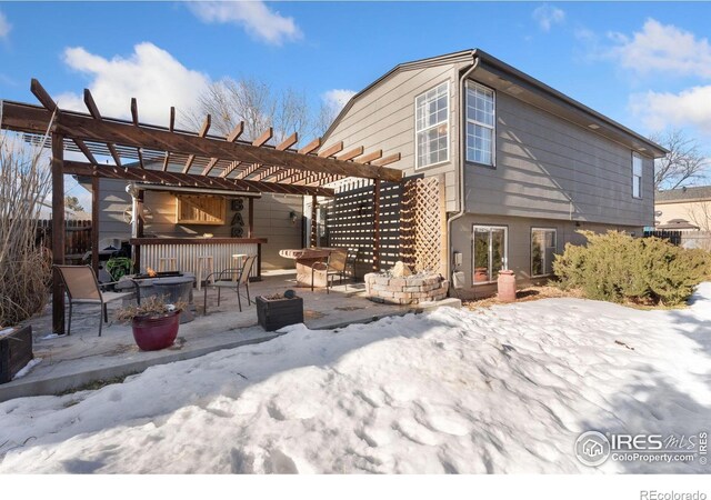 snow covered rear of property featuring a pergola, an outdoor fire pit, a patio, and exterior bar