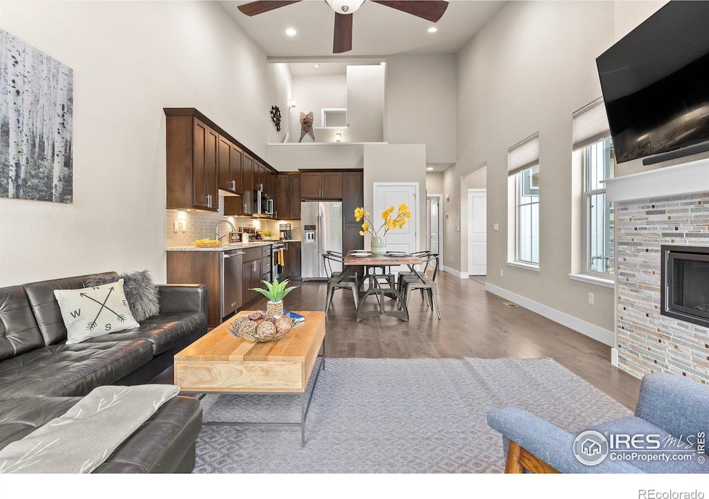 living room featuring a towering ceiling, dark hardwood / wood-style floors, sink, a tiled fireplace, and ceiling fan