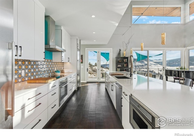 kitchen with appliances with stainless steel finishes, white cabinetry, backsplash, a mountain view, and wall chimney exhaust hood