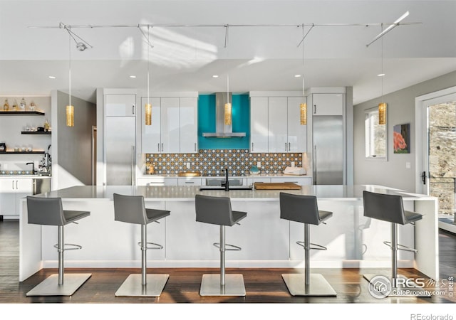 kitchen with sink, a breakfast bar, hanging light fixtures, white cabinets, and wall chimney exhaust hood