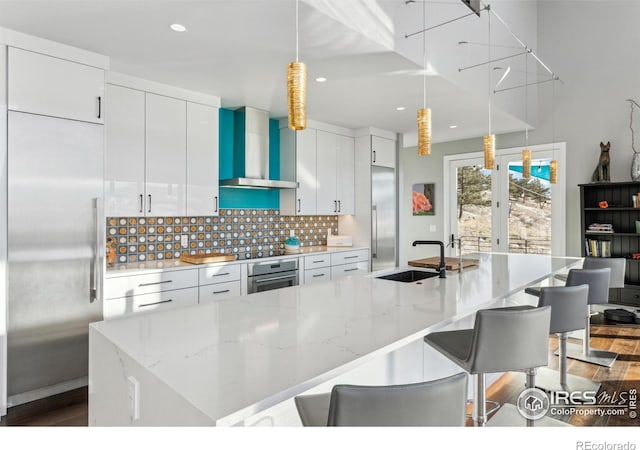 kitchen with pendant lighting, wall chimney range hood, sink, appliances with stainless steel finishes, and white cabinets