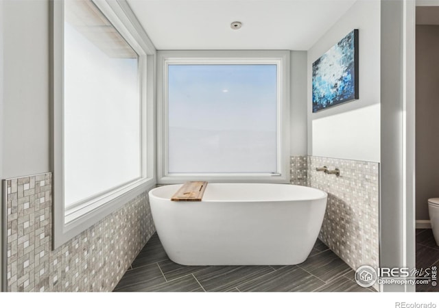 bathroom featuring a healthy amount of sunlight, toilet, a bathing tub, and tile walls