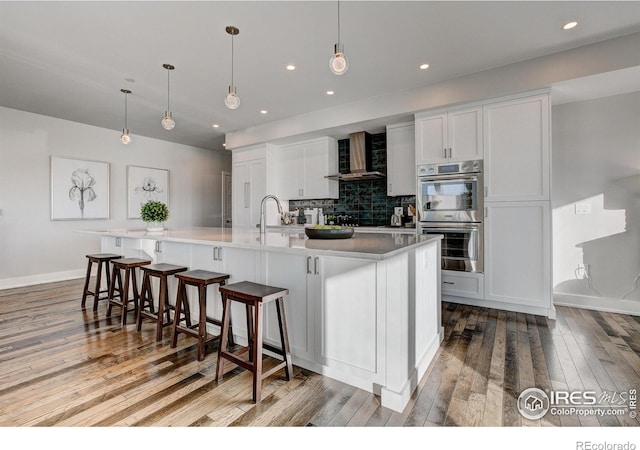 kitchen with a large island, white cabinets, decorative light fixtures, and wall chimney exhaust hood