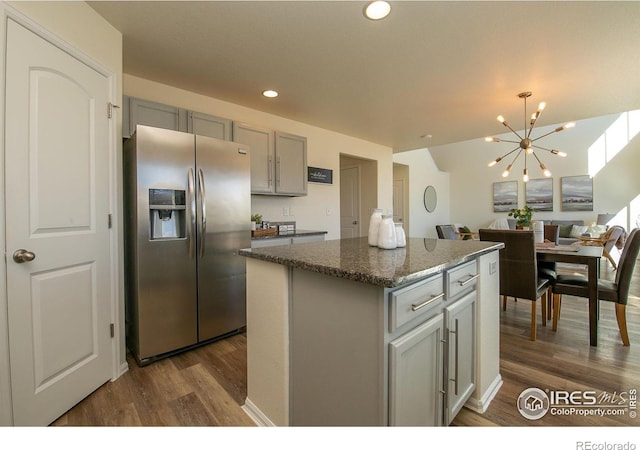 kitchen with stainless steel fridge, gray cabinetry, dark stone countertops, a notable chandelier, and a kitchen island