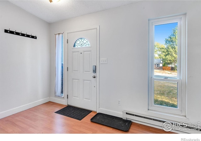 foyer entrance featuring a baseboard heating unit, a textured ceiling, and light wood-type flooring